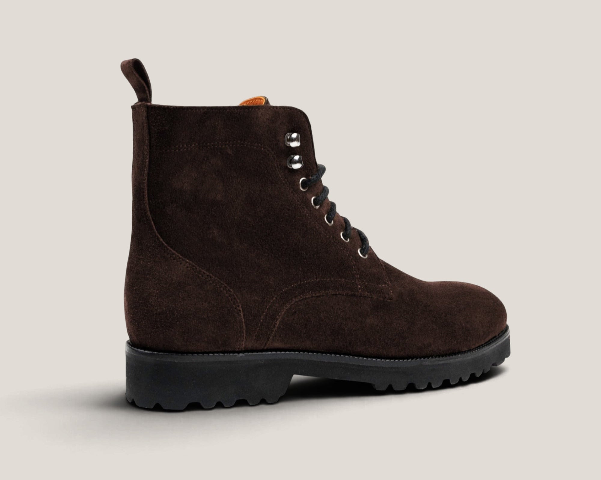 A dark brown suede lace-up boot with a black lug sole, shown from a side profile against a light beige background.