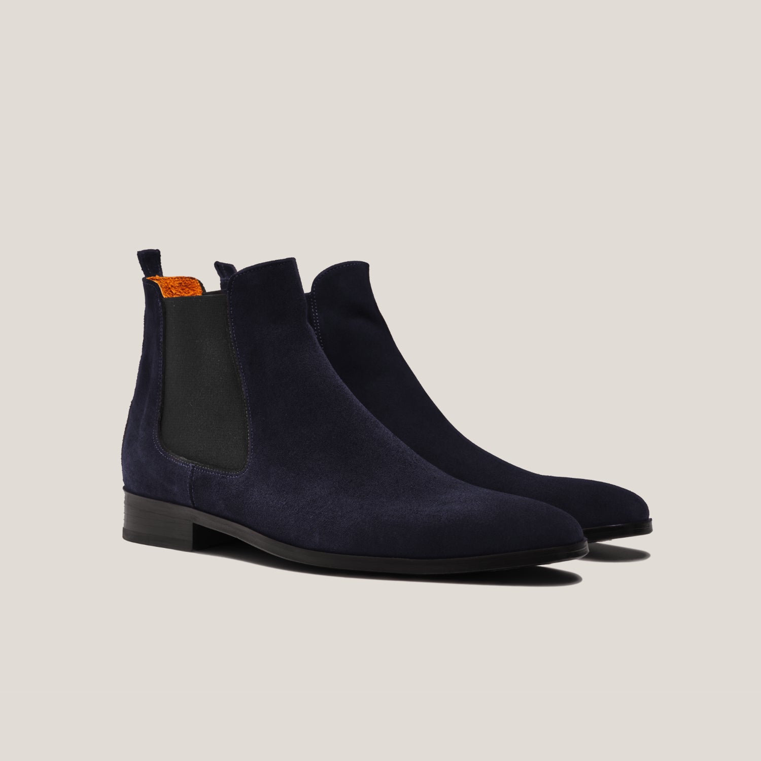 Pair of navy blue suede Chelsea boots on a light beige background