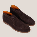 A pair of dark brown suede chukka-style shoes with matching laces and a contrasting tan sole, displayed on a light beige background.