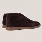A pair of dark brown suede chukka boots with a brown rubber sole, shown from a side profile view against a light beige background.