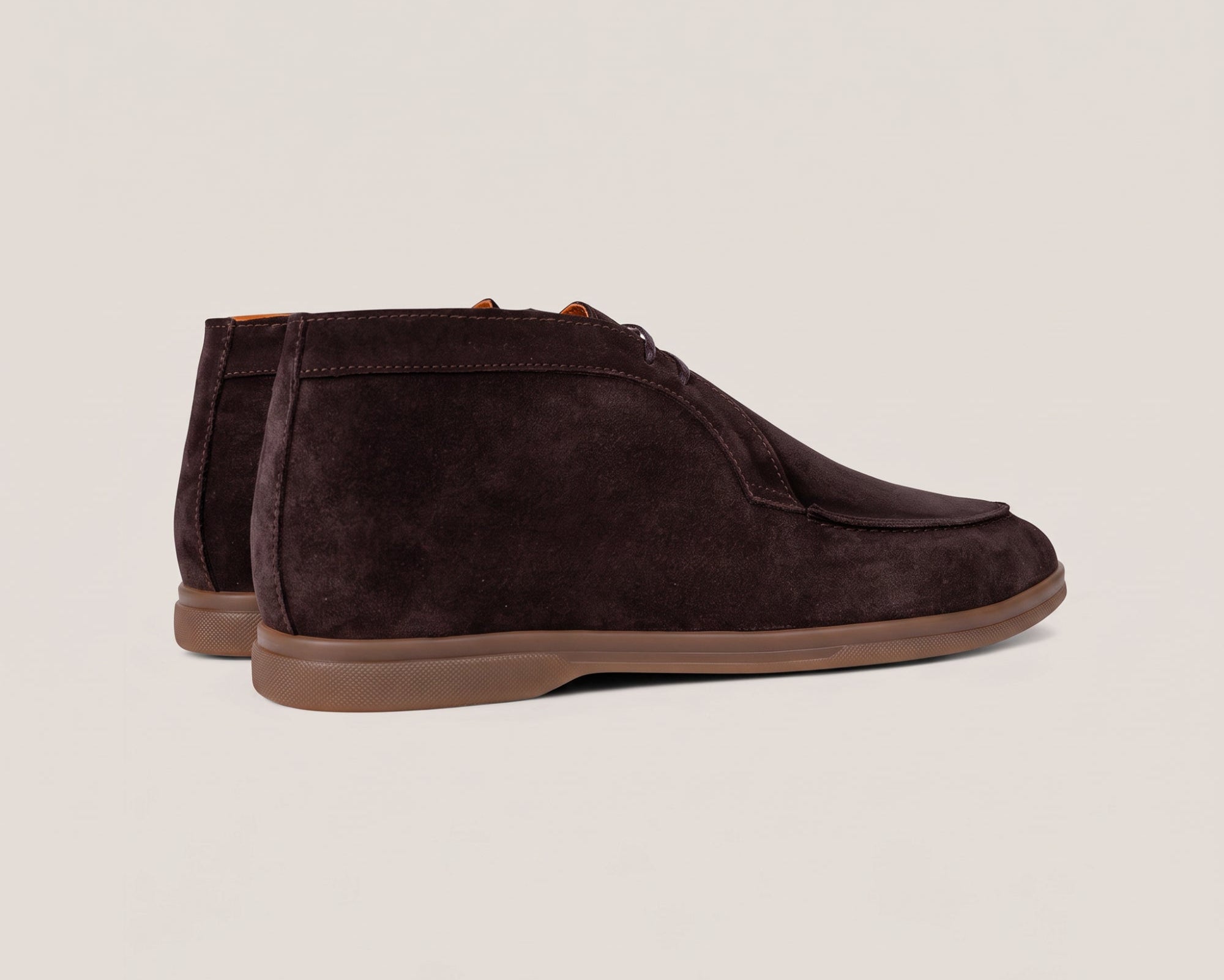 A pair of dark brown suede chukka boots with a brown rubber sole, shown from a side profile view against a light beige background.