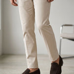 A man wearing slim-fit beige trousers, a brown shirt, and dark brown suede penny loafers, shown from the waist down in a minimalist indoor setting. Rapallo Dark brown suede handmade penny loafer Reinhard frans