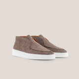 Pair of brown suede shoes with white soles on a beige background